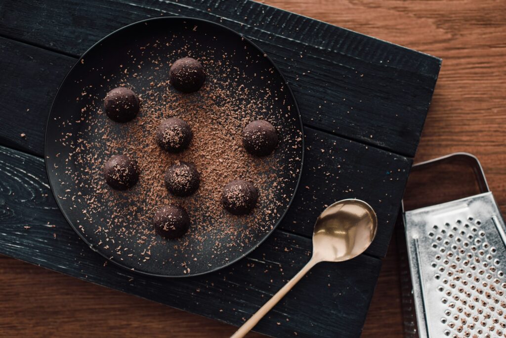 top view of cutting board with truffles on plate covering by grated chocolate, spoon and grater on